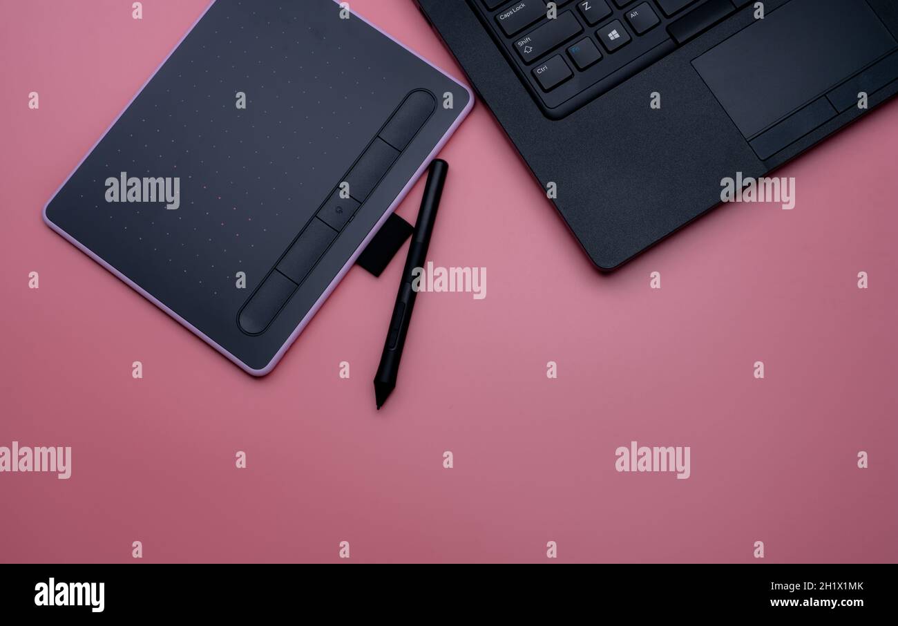 Top view of black pen mouse, digital tablet, and laptop for graphic design work on pink background. Above view of pen graphic tablet. Gadget for graph Stock Photo