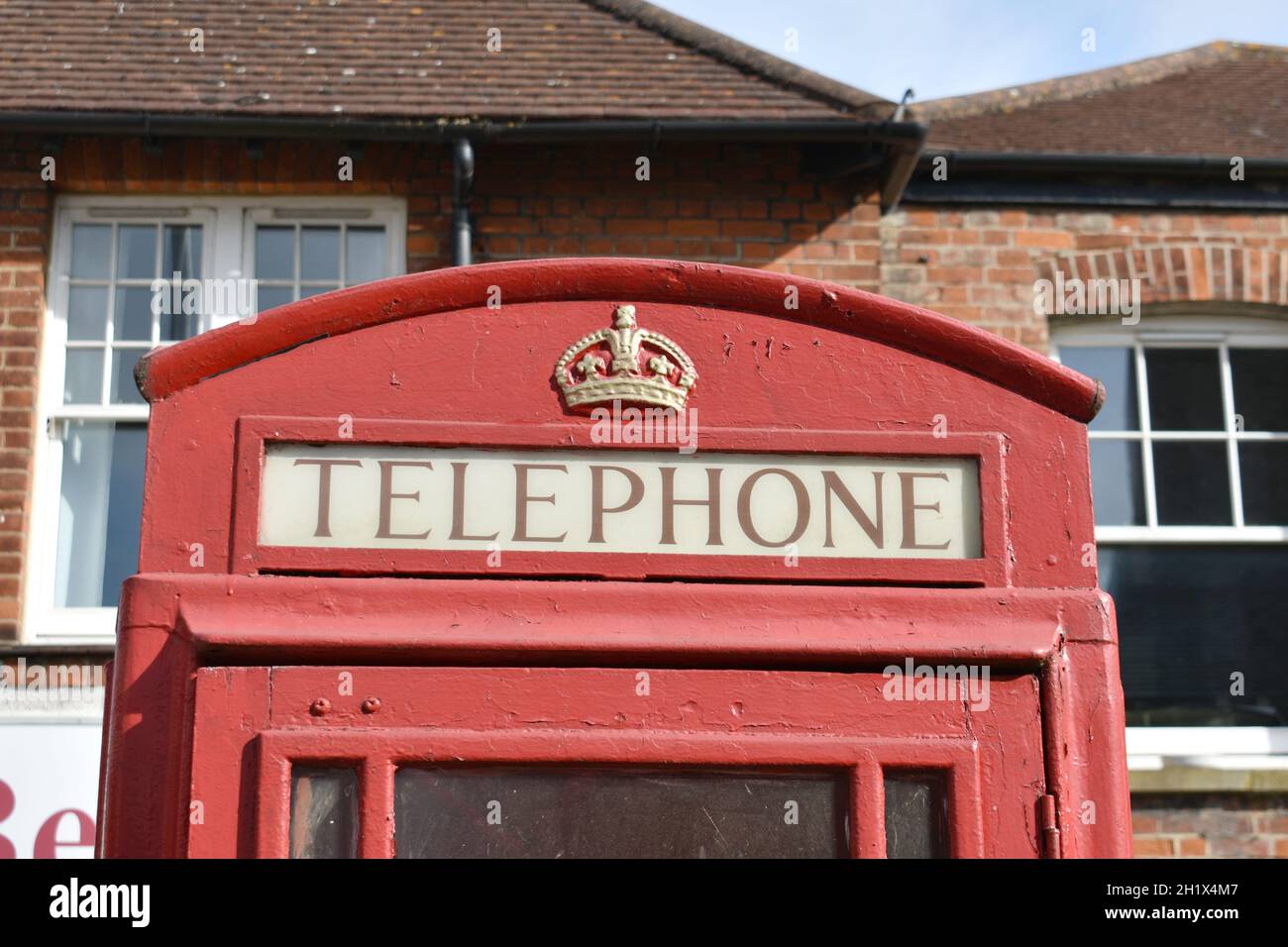 close up of  vintage red telephone box with gold royal crown on top,  outside in a  street in front of a brick building in summer Stock Photo