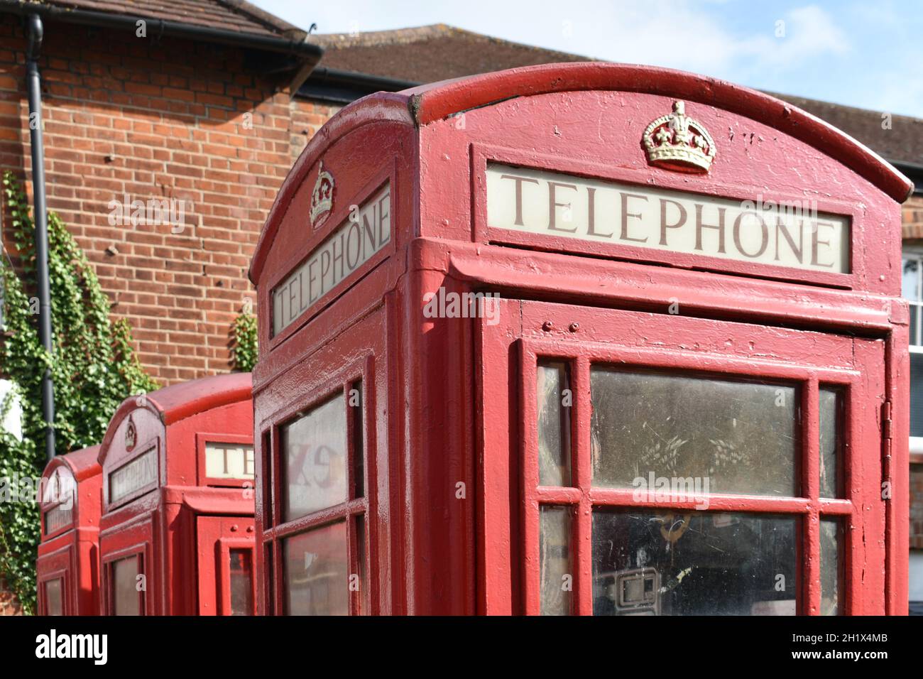 close up of 3 vintage red telephone boxes with gold royal crown on top, in a street outside a brick building in summer Stock Photo