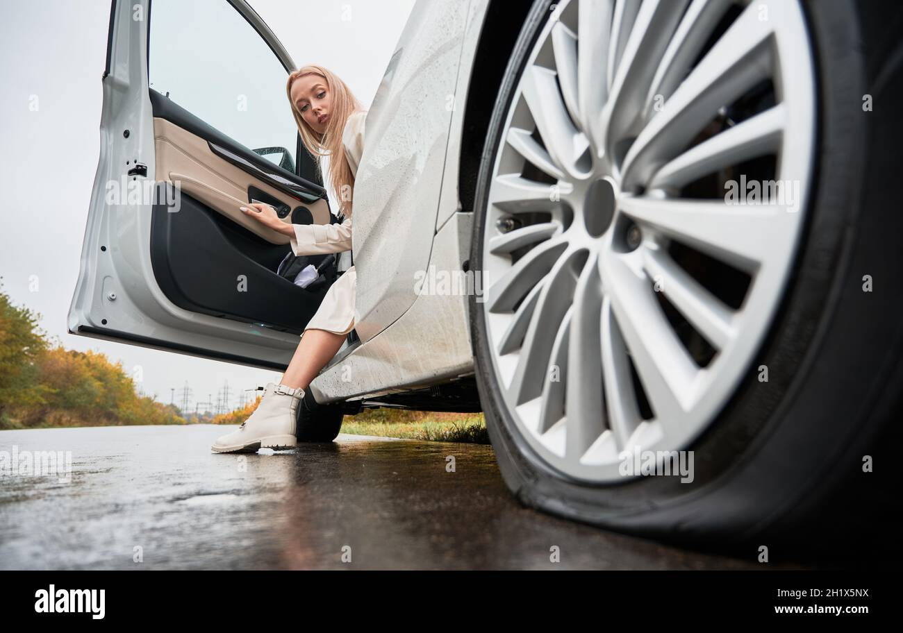 Beautiful woman on a road stopped her white car with punctured car tire