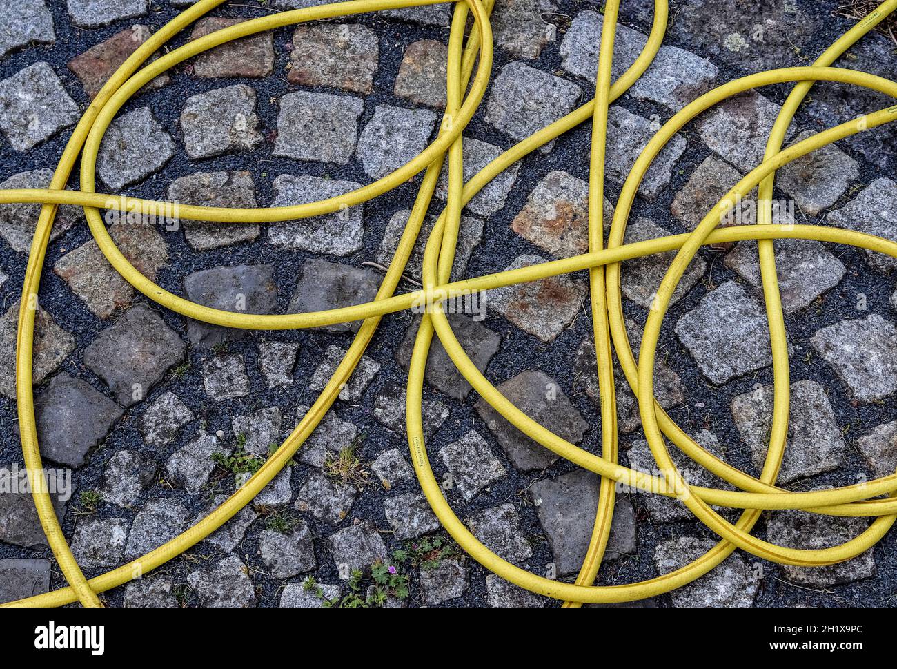 Top view of hosepipe on grass and cobblestone surfaces. Minimalistic conception. Stock Photo