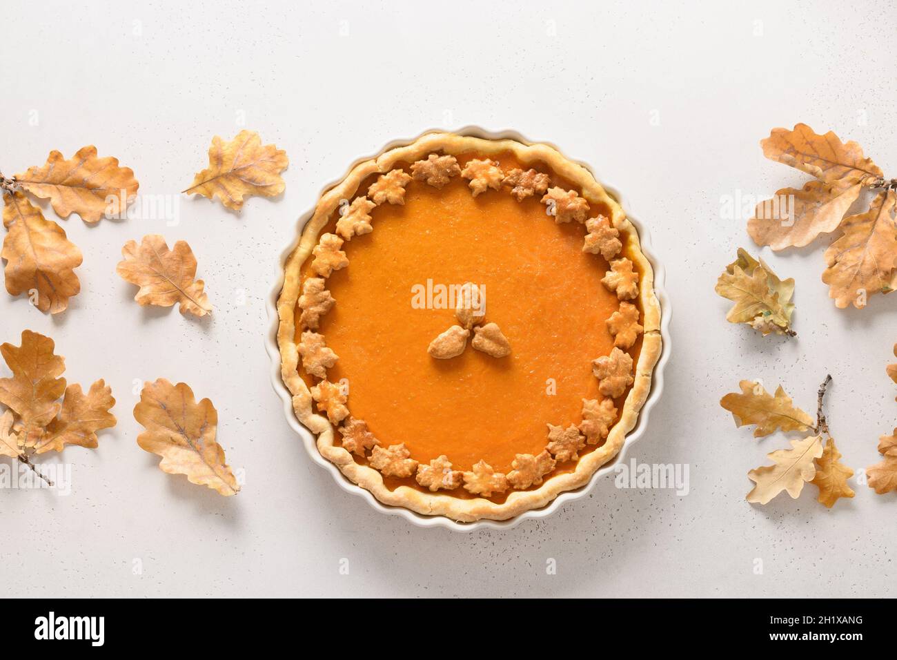 Homemade tasty Pumpkin Pie with autumn oak leaves for Thanksgiving Day on white background. View from above. Flat lay. Banner Fall. Stock Photo