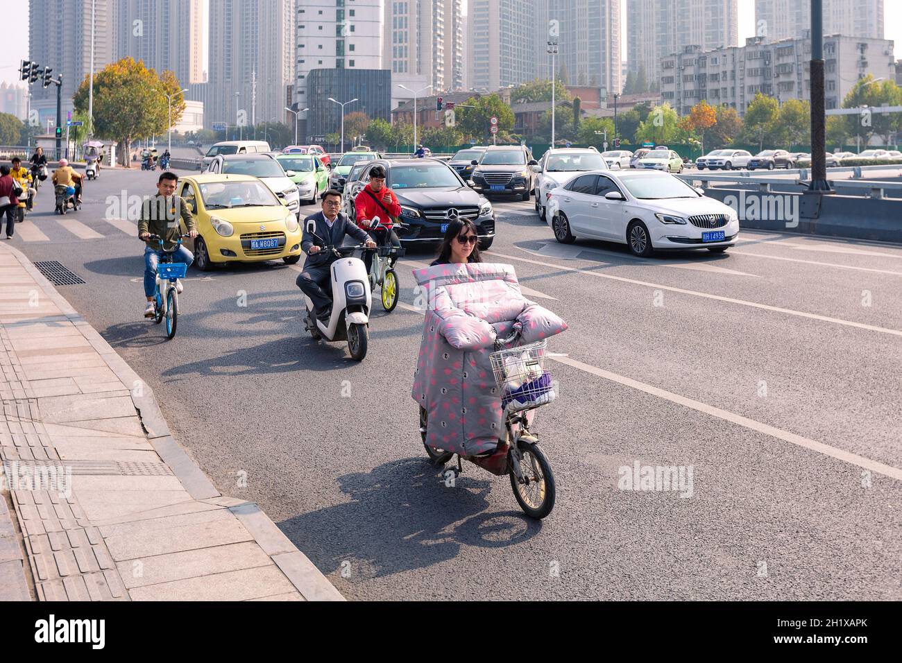 Hefei, China - November 5, 2019: People on electric bicycle on crossroad. The weather became cold and each electric bike was fitted with colorful wind Stock Photo