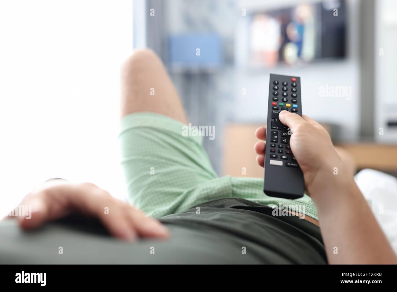 Man lies on bed and switches buttons on TV remote control Stock Photo
