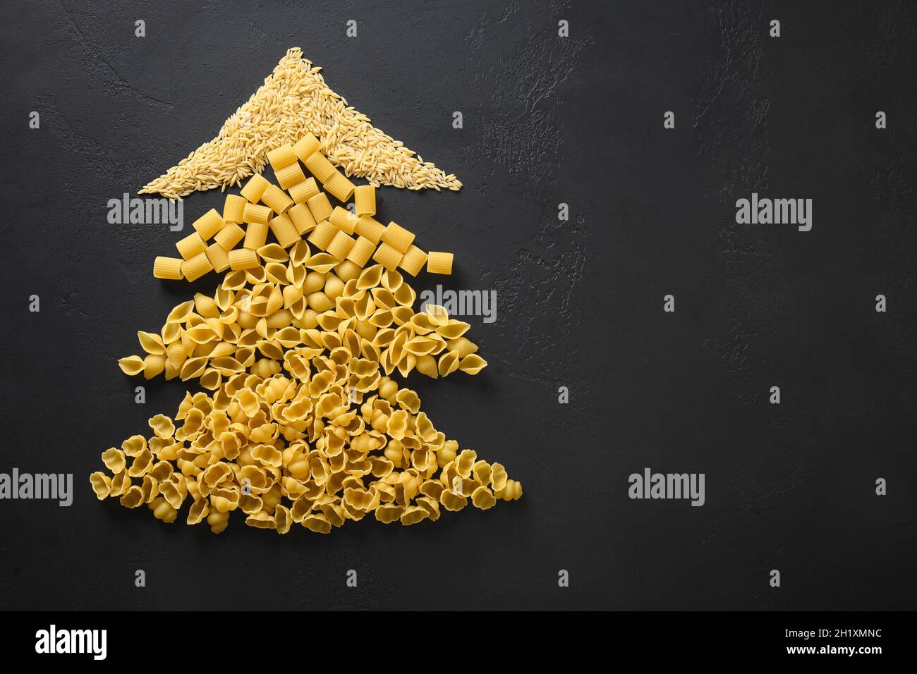 Alternative creative Christmas tree of different dry pasta on black background. Xmas greeting card with copy space. View from above. Food holiday conc Stock Photo