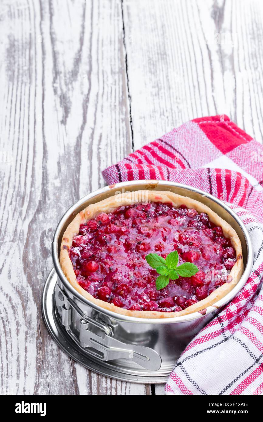 Freshly baked red currant pie in baking form on white wooden table ...