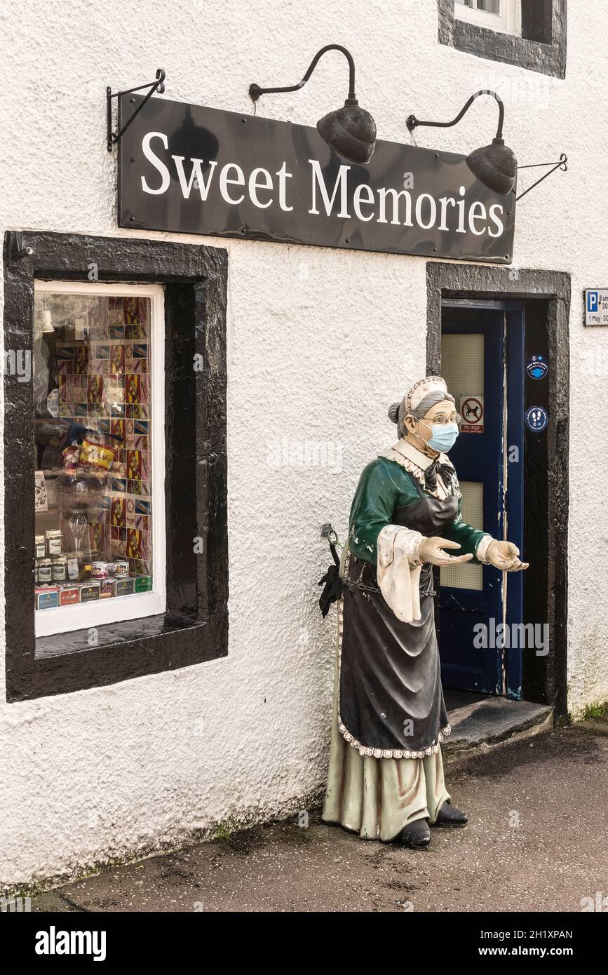 A mask-wearing model of a shopkeeper at Sweet Memories, a traditional shop in Inveraray, Scotland, UK, selling old-fashioned sweets and confectionery Stock Photo