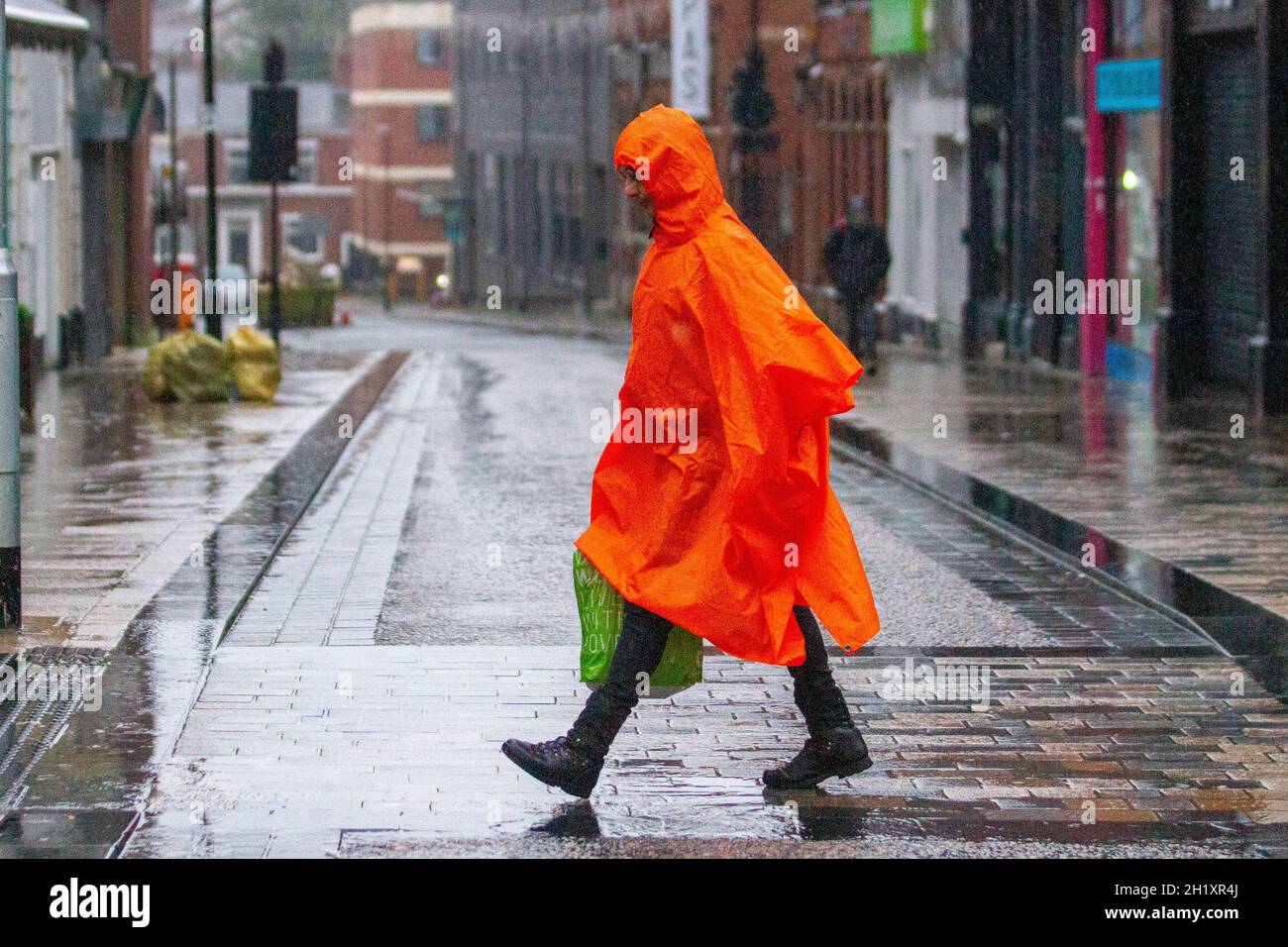 Man wearing full length orange waterproof plastic mac in Preston, Lancashire. UK 19 Oct 2021. Shops, shoppers shopping on a wet gusty day in Preston city centre. Credit:MediaWorldImages/AlamyLiveNews Stock Photo