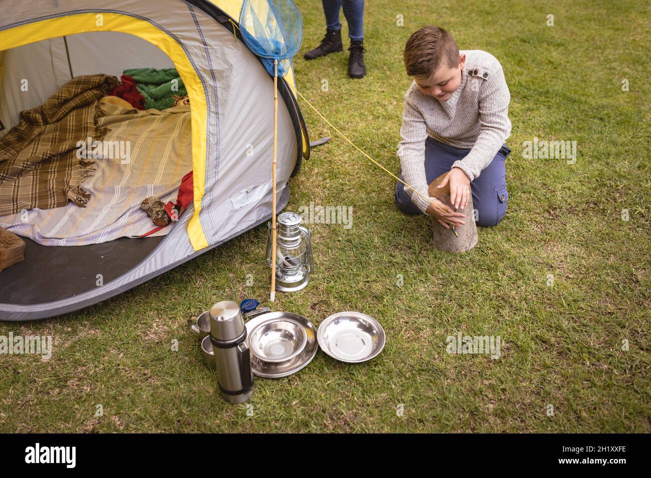 Caucasian boy setting up a tent by tying the strings to a tree log in the garden Stock Photo