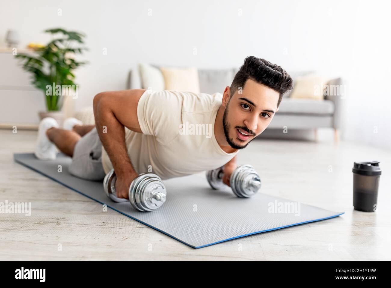 Stay at home fitness. Strong young Arab man doing whole body workout standing in plank pose using dumbbells indoors Stock Photo Alamy