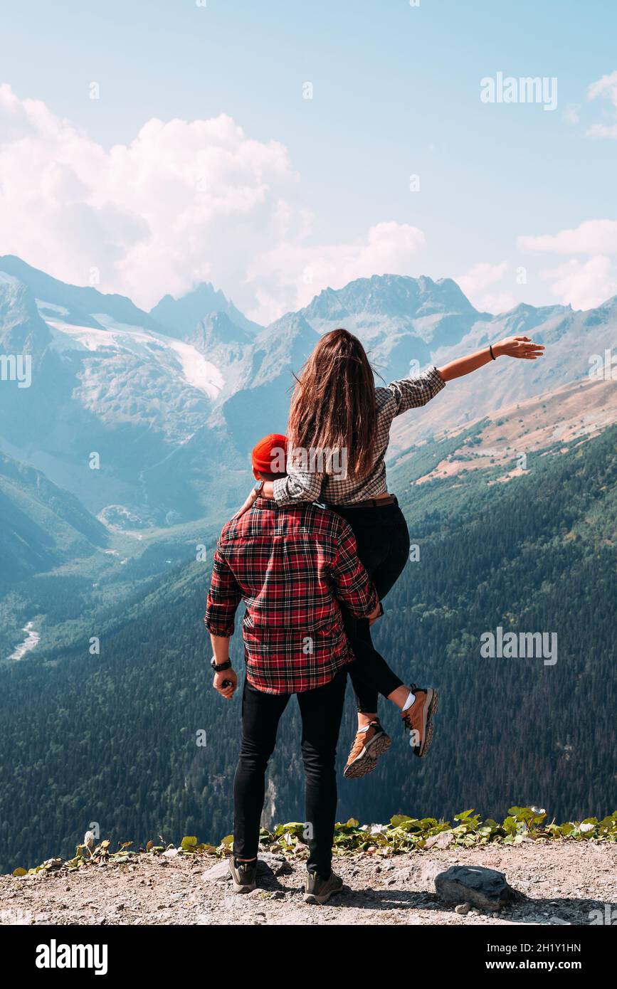 Beautiful couple among the mountains. A couple in love in the mountains, back view. The man lifted the woman into his arms. Hiking in the mountains Stock Photo
