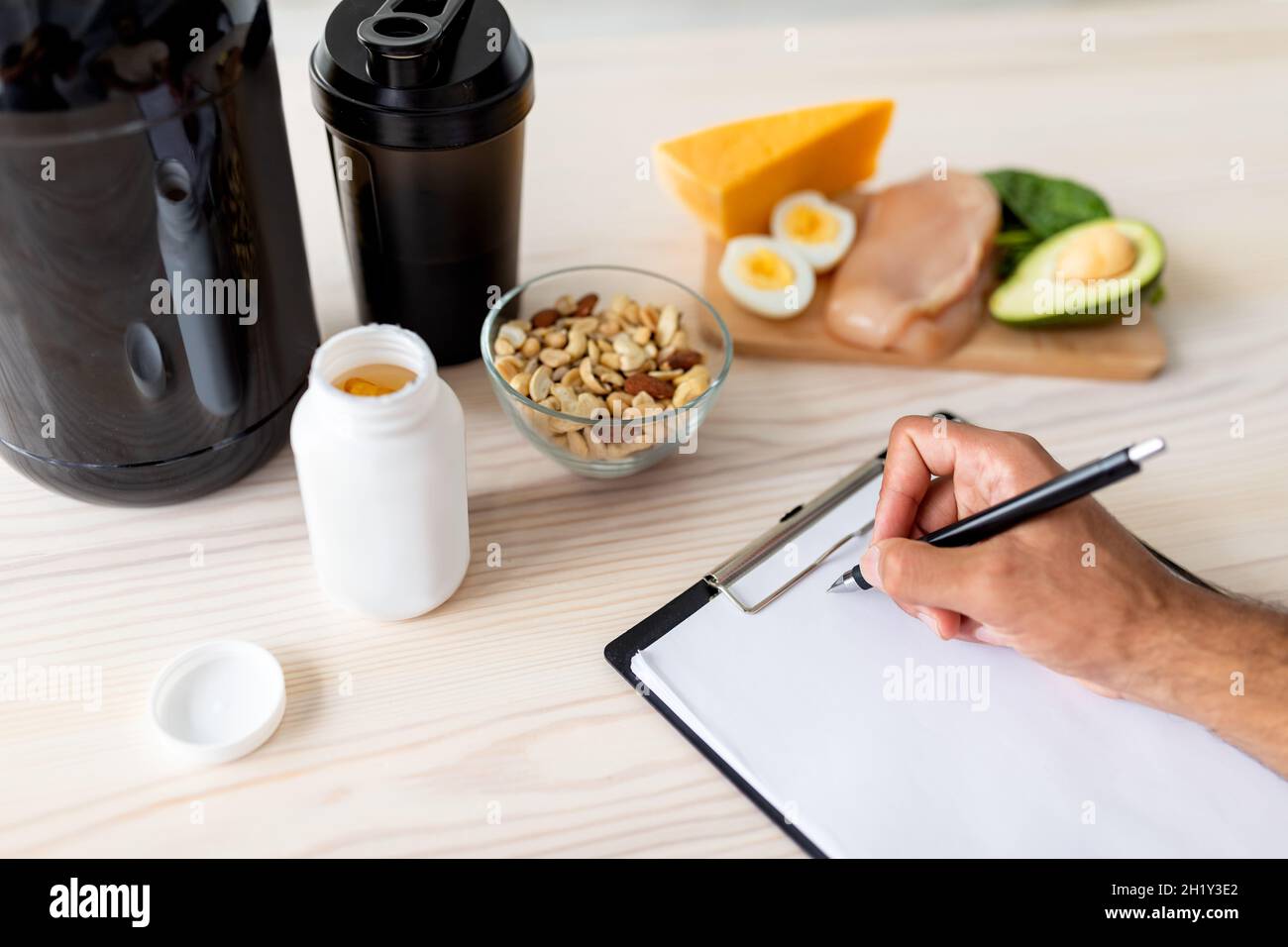 Closeup of young bodybuilder writing meal plan on clipboard with mockup, eating healthy foods, using protein shakes Stock Photo