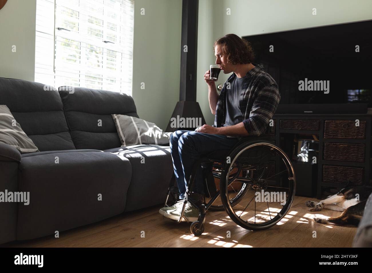 Thoughtful caucasian disabled man sitting on wheelchair drinking coffee at home Stock Photo