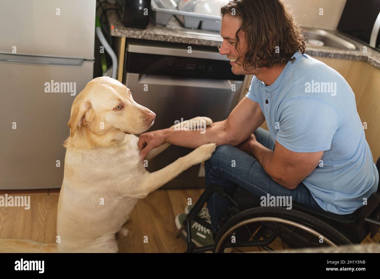 Caucasian disabled man sitting on wheelchair playing with dog at home Stock Photo