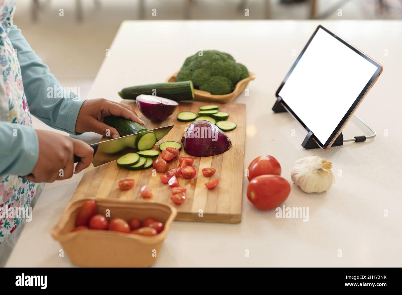 Hands of african american woman using tablet with copy space and cutting vegetables in kitchen Stock Photo