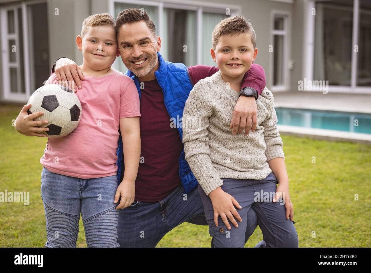 Portrait of caucasian father and two sons smiling while holding football in the garden Stock Photo