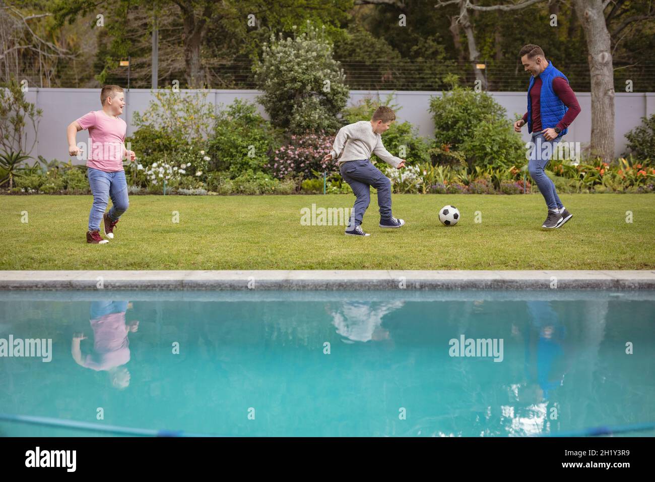 Caucasian father and two sons playing football together in the garden Stock Photo