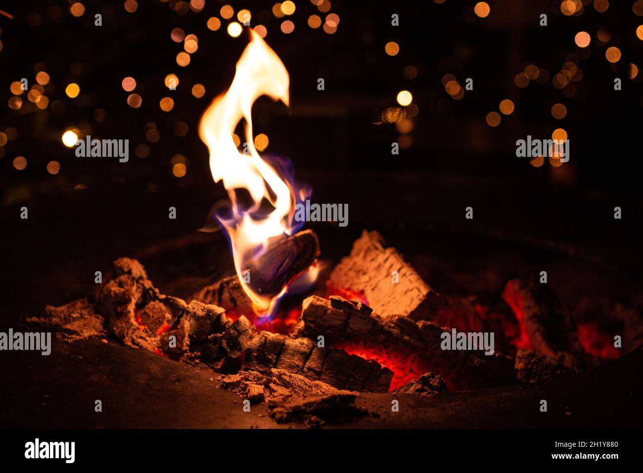 close up of fireplace with burning fire wood in cold winter night and bokeh christmas lights at traditional christmas market at Merano, South Tyrol Stock Photo