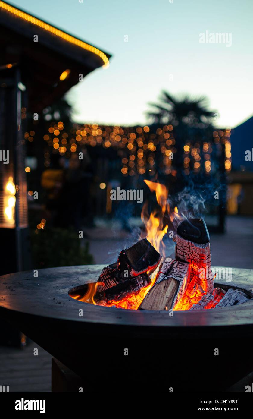 close up of fireplace with burning fire wood in cold winter night and bokeh christmas lights at traditional christmas market at Merano, South Tyrol Stock Photo