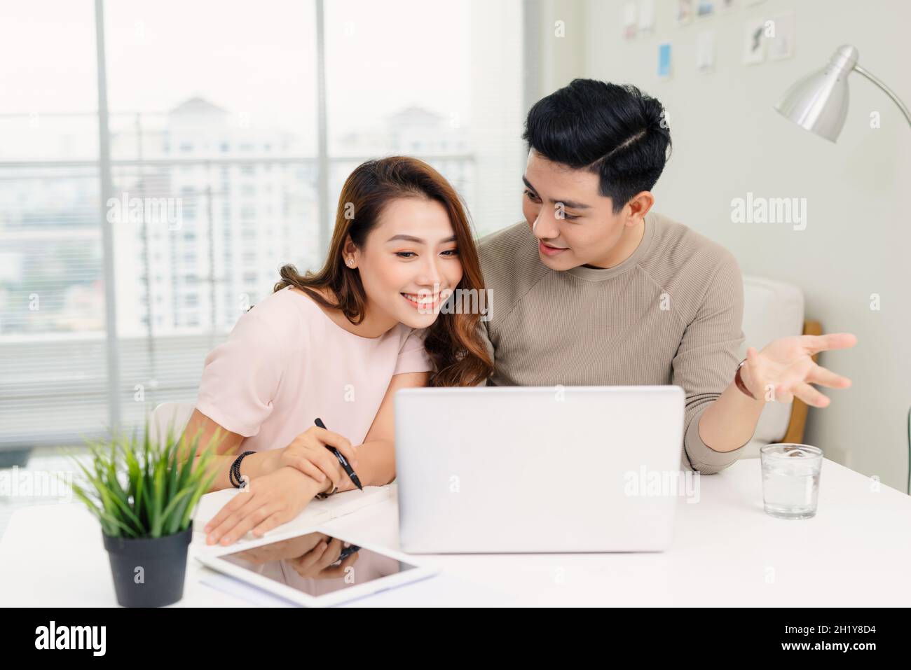 Positive hipster couple having fun while working together remotely at home using modern technology Stock Photo