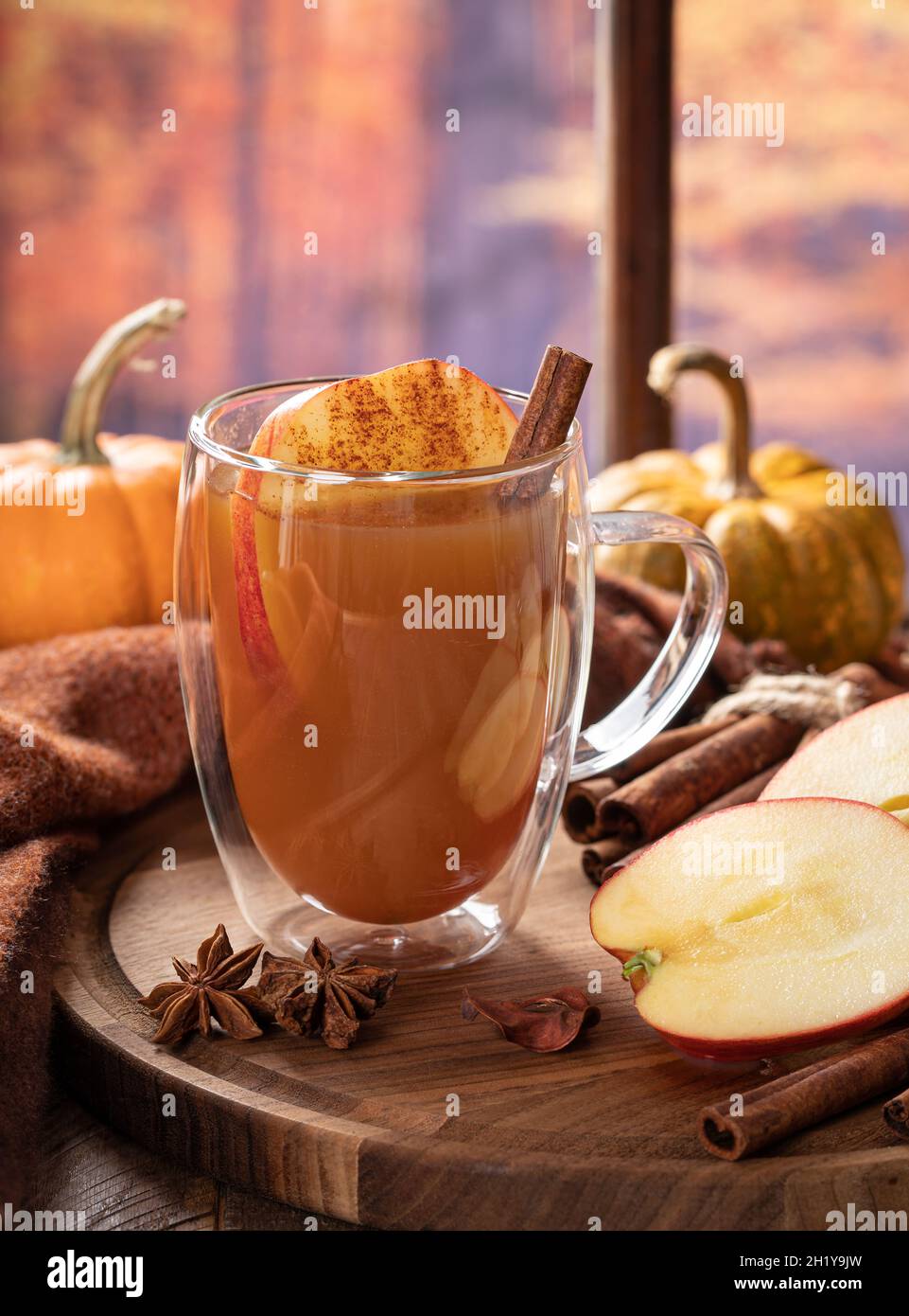 Cup of apple cider and sliced apples on a wooden platter with pumpkins ...