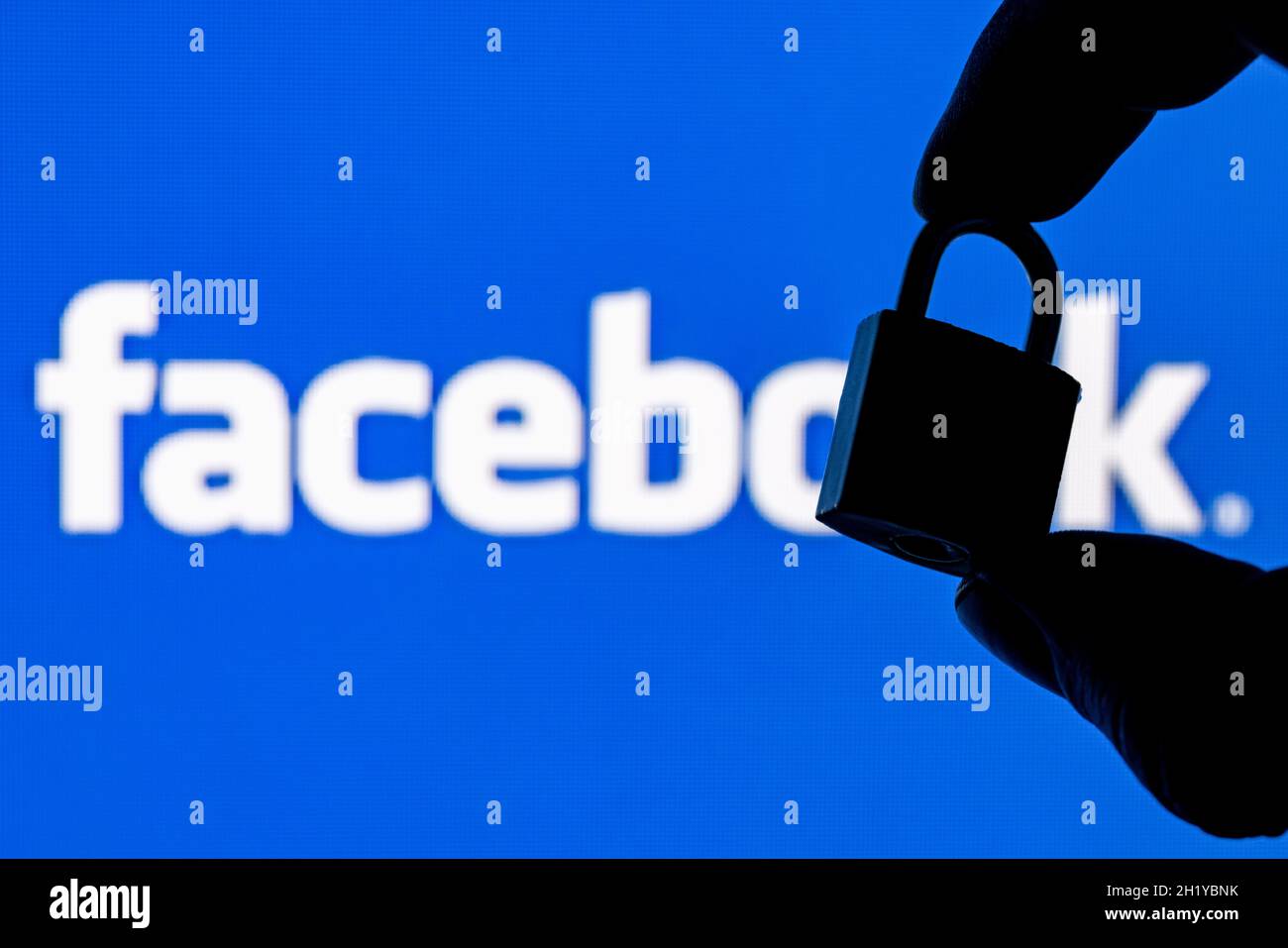 Fingers hold a closed security lock on the background of the facebook social network logo. The concept of data security in Facebook. Stock Photo