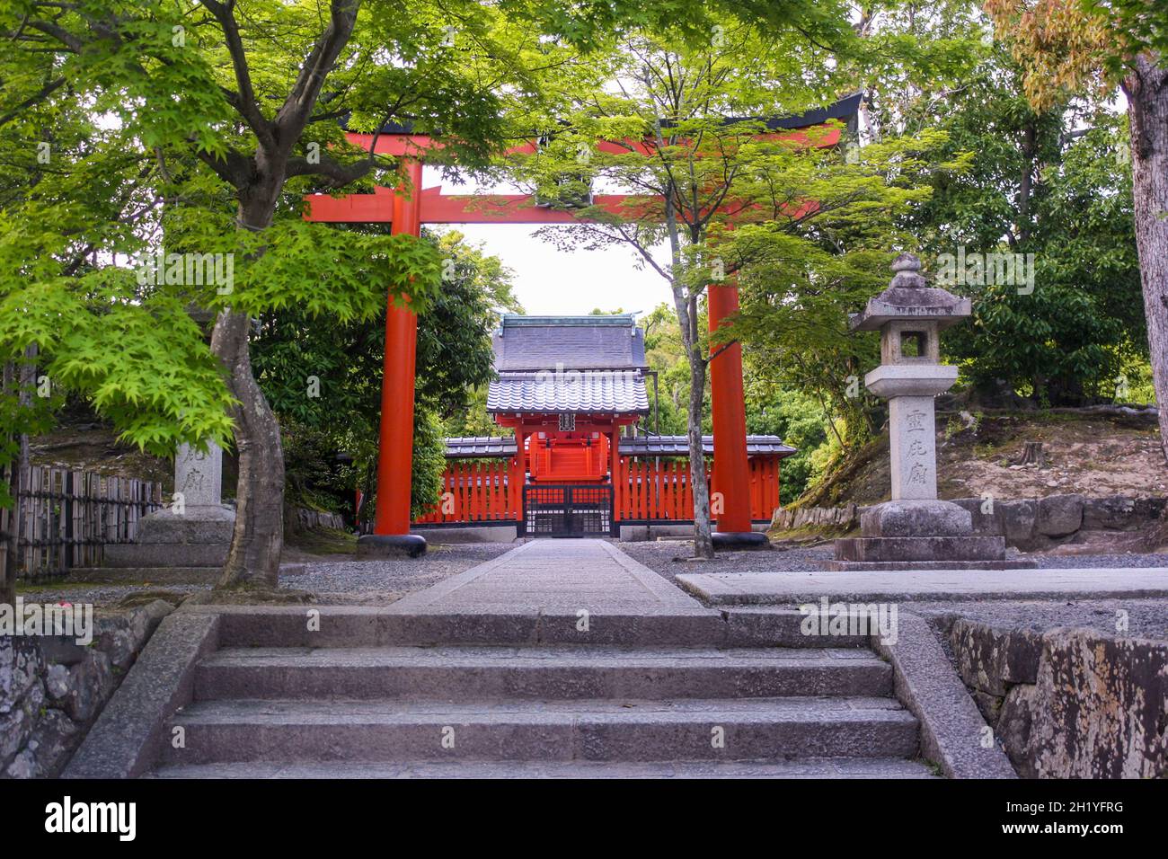 Ancient shrine dedicated to Hachiman Daibosatsu with large red torii gate and surrounded by trees in the zen garden of Tenryuji Temple at Arashiyama. Stock Photo