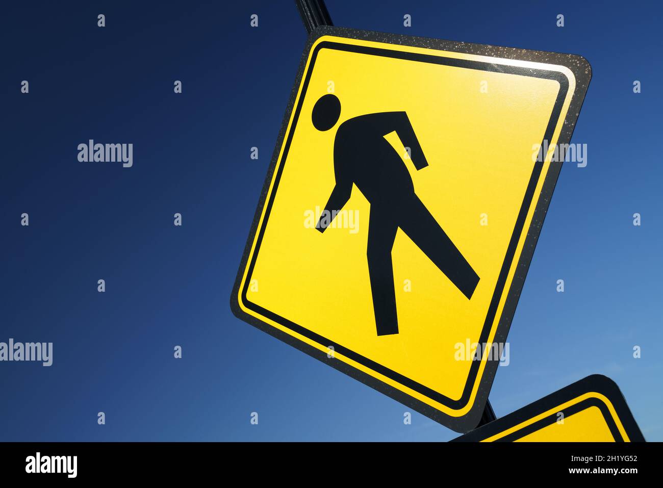 A bold and colorful scene, with a bright yellow 'pedestrian crossing' street sign (showing a human form walking) contrasted against a deep blue sky. Stock Photo