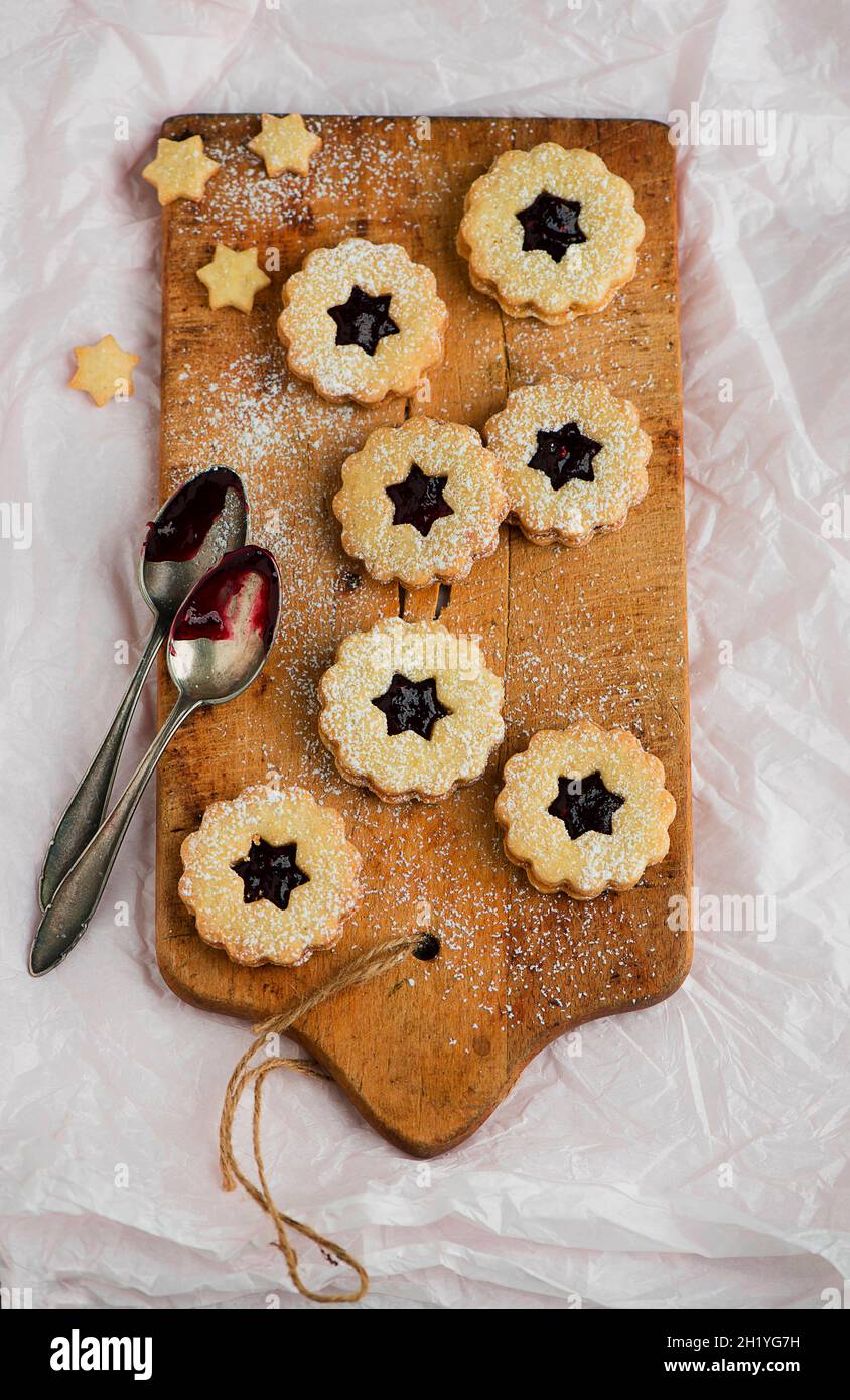 Linzer Plätzchen (nutty shortcrust jam sandwich biscuits with holes on top) on a wooden board Stock Photo