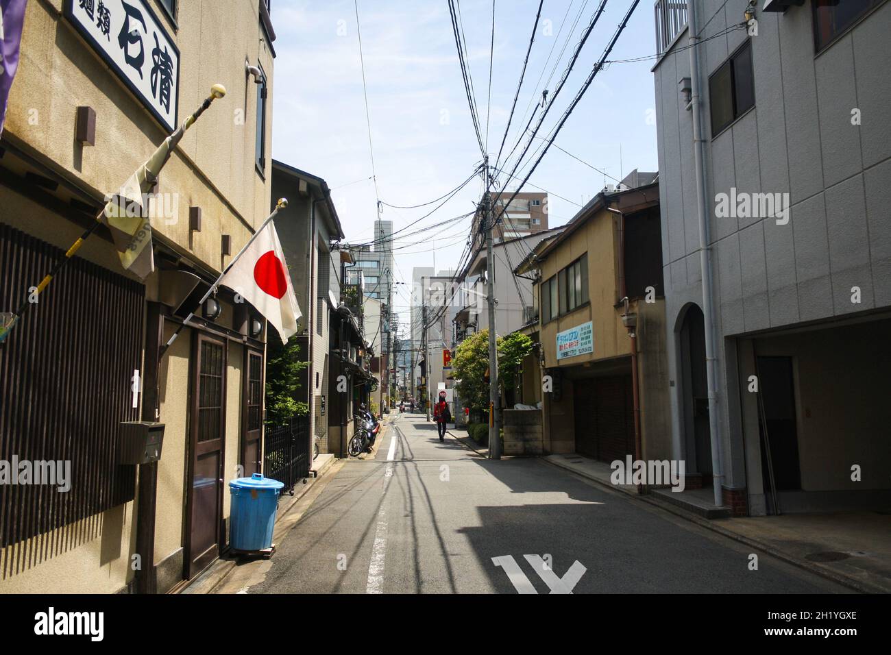 An alley in downtown Kyoto with small houses and electrical network cable. National flag of Japan or hinomaru on one of the house. Cloudy blue sky. Stock Photo