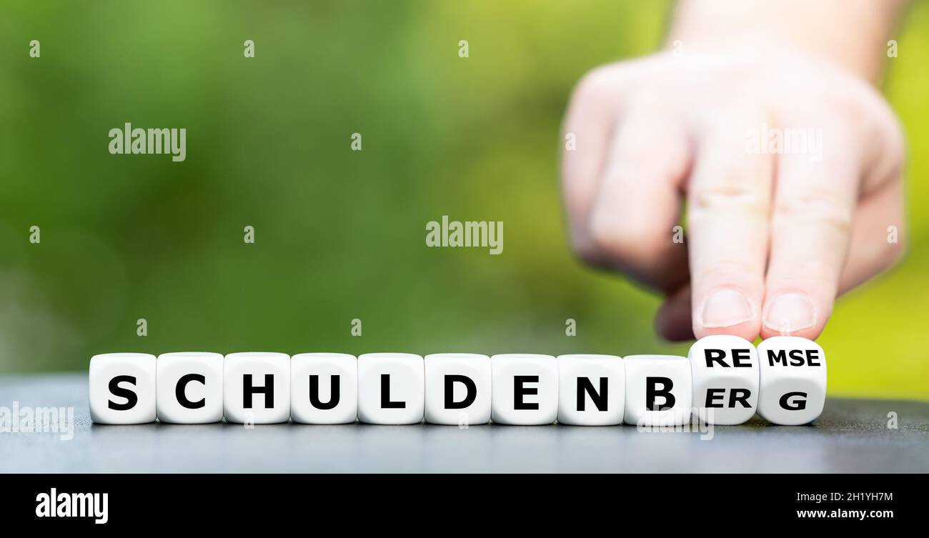 Hand turns dice and changes the German word 'Schuldenberg' (mountain of debt) to Schuldenbremse' (debt brake). Stock Photo