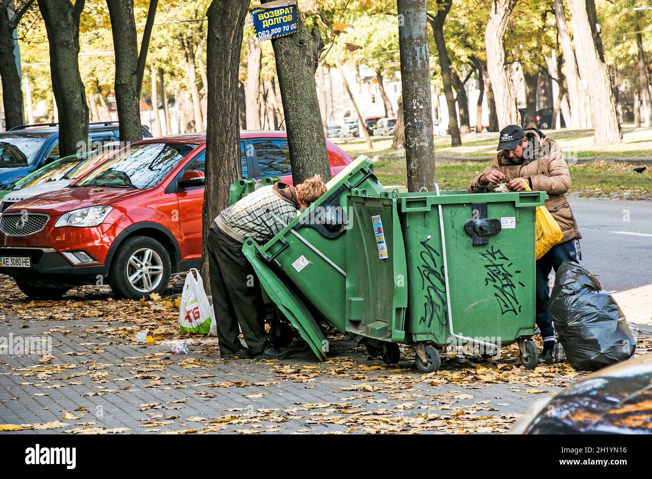 Dnepropetrovsk, Ukraine - October 15, 2021: Homeless people are looking for food in a dumpster. Selective focus, street photo, urban poverty. Stock Photo