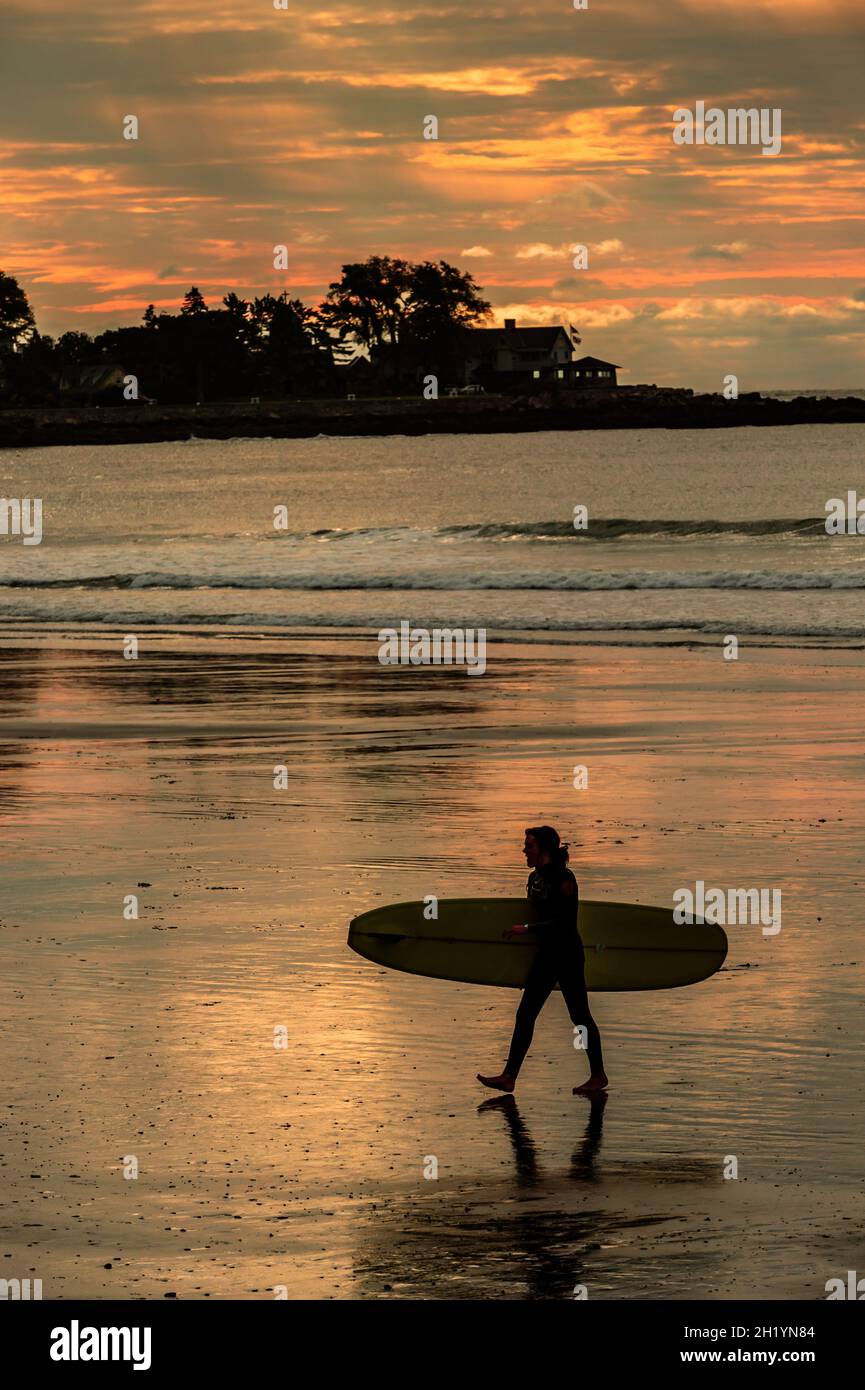 As the sun starts to rise through the clouds, this very weary surfer heads home for a rest, before going out to ride the waves at high tide. Stock Photo