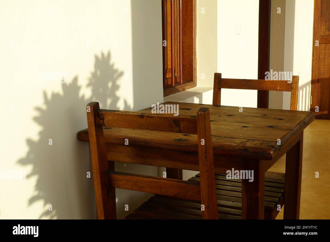 A white wall in the warm sunlight, two wooden chairs and a table, and ...