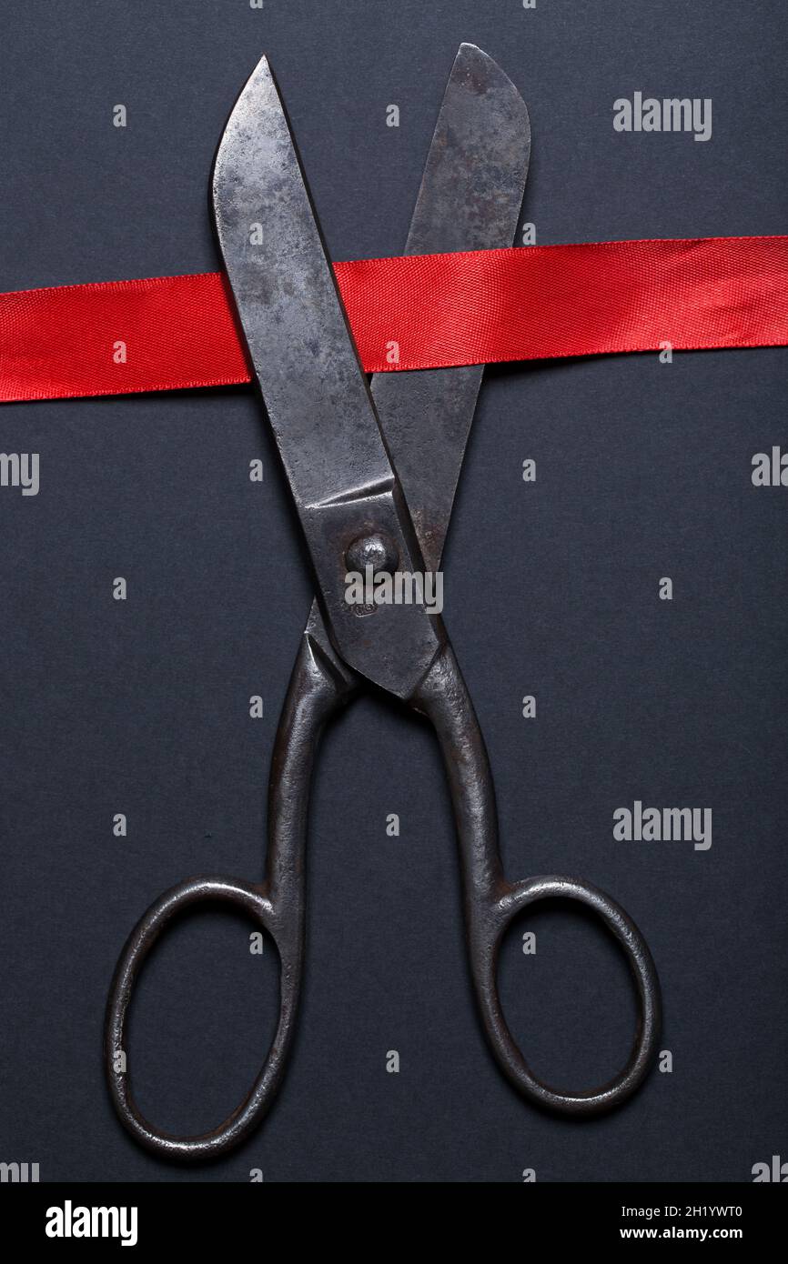 High angle view of vintage scissors cutting red ribbon on black background. Stock Photo