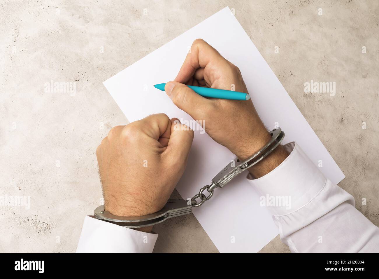 A man in handcuffs writes a will or confession of a crime, the concept of obtaining consent under the influence of pressure on people Stock Photo