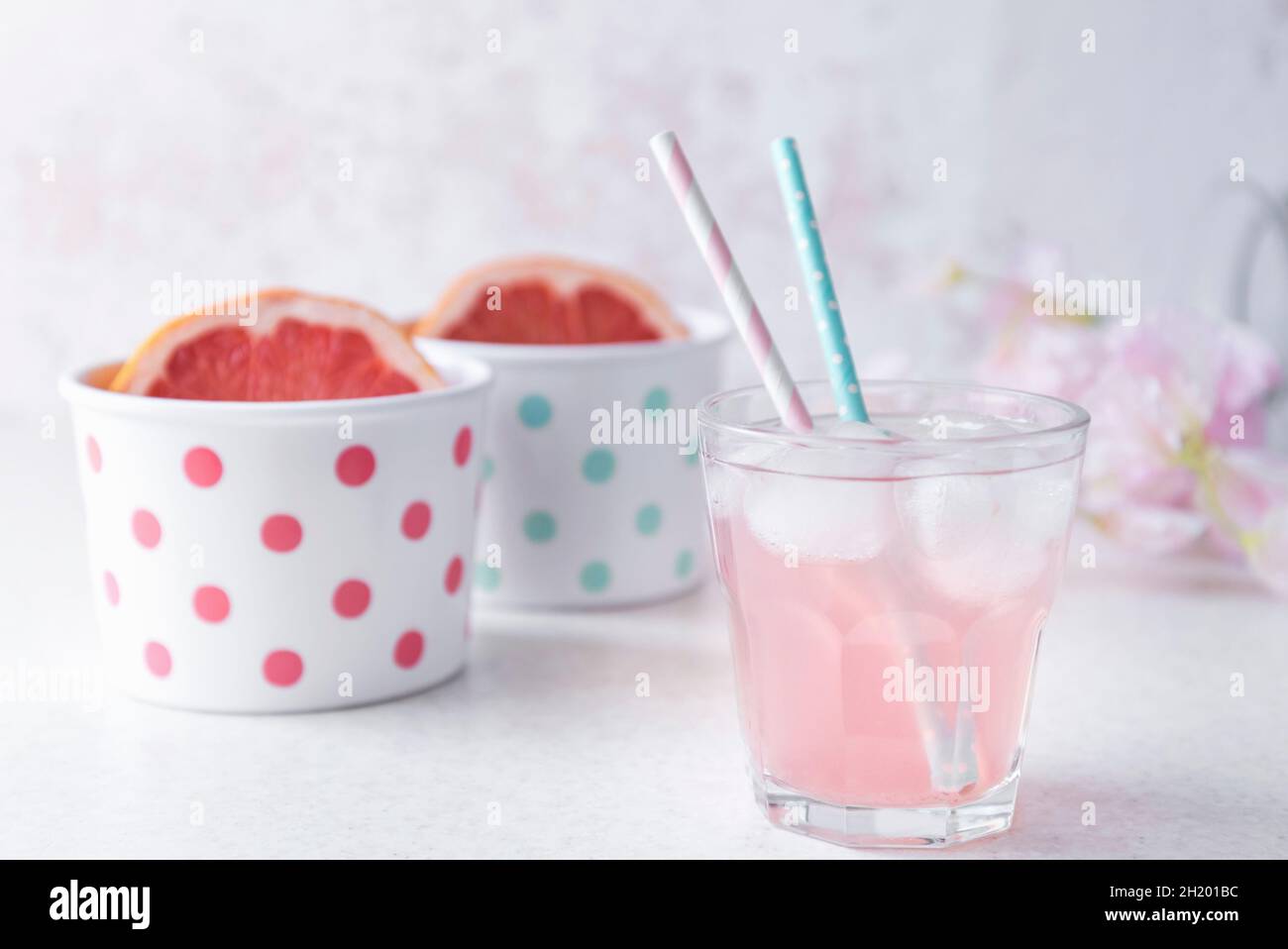 A glass of pink colored grapefruit infused water with pastel colored beverage straws, halved grapefruit in polka dotted bowls Stock Photo