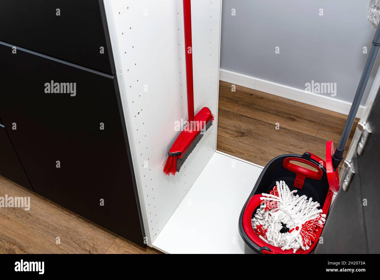 A broom hanging in a builtin kitchen cupboard and a mop with a bucket