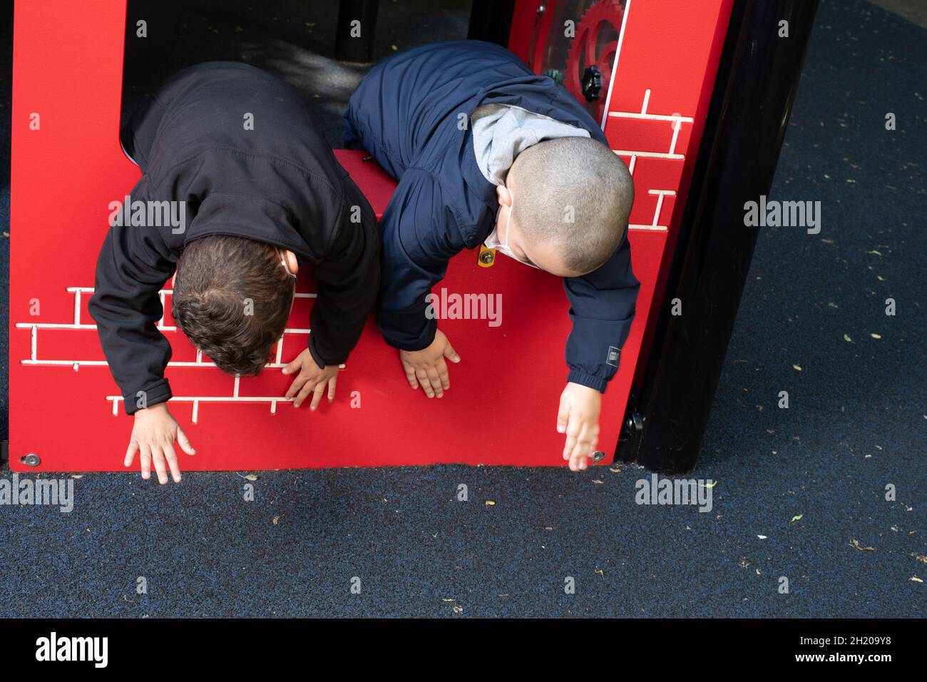 Education Preschool 3-4 year olds two boys leaning over edge of playground equipment to slap their hands on its surface Stock Photo