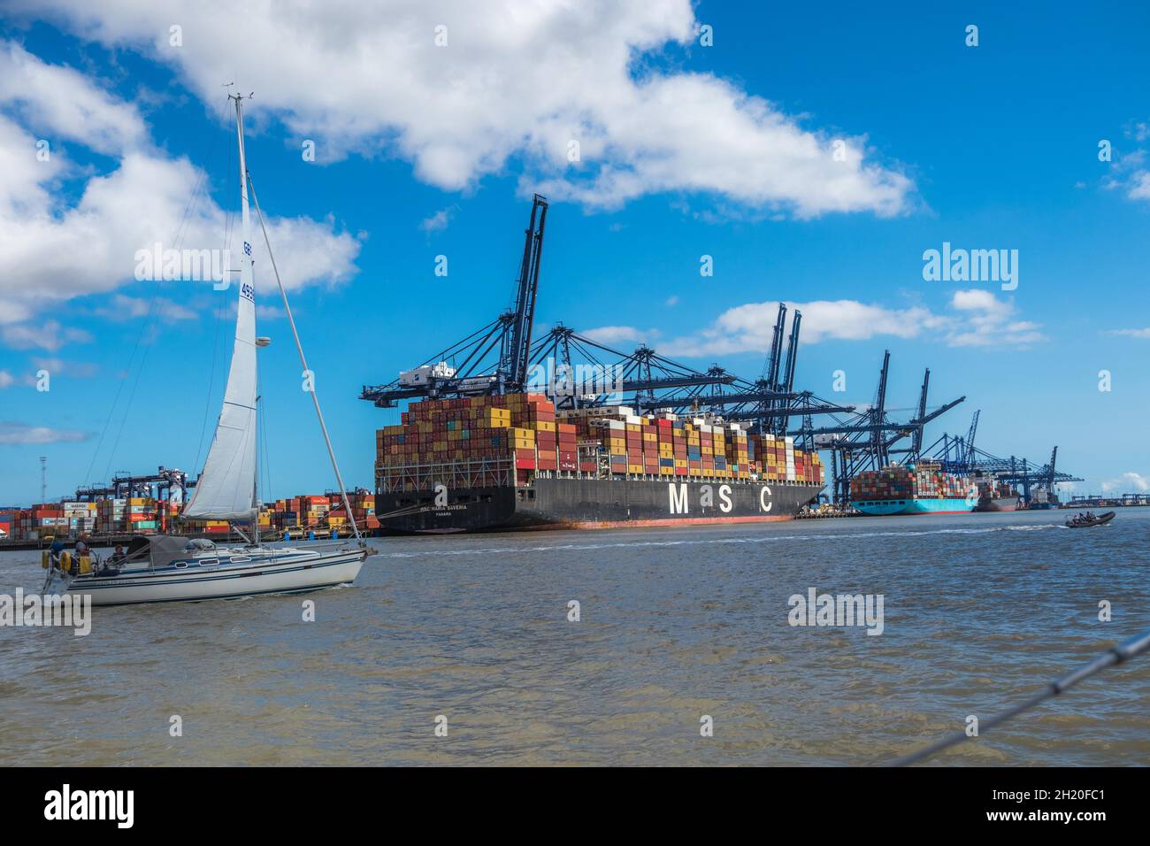 Yacht sailing pass MSC container ship Maria Saveria alongside Trinity Terminal a container handling facility with Ship-to-Shore cranes at Felixstowe Stock Photo