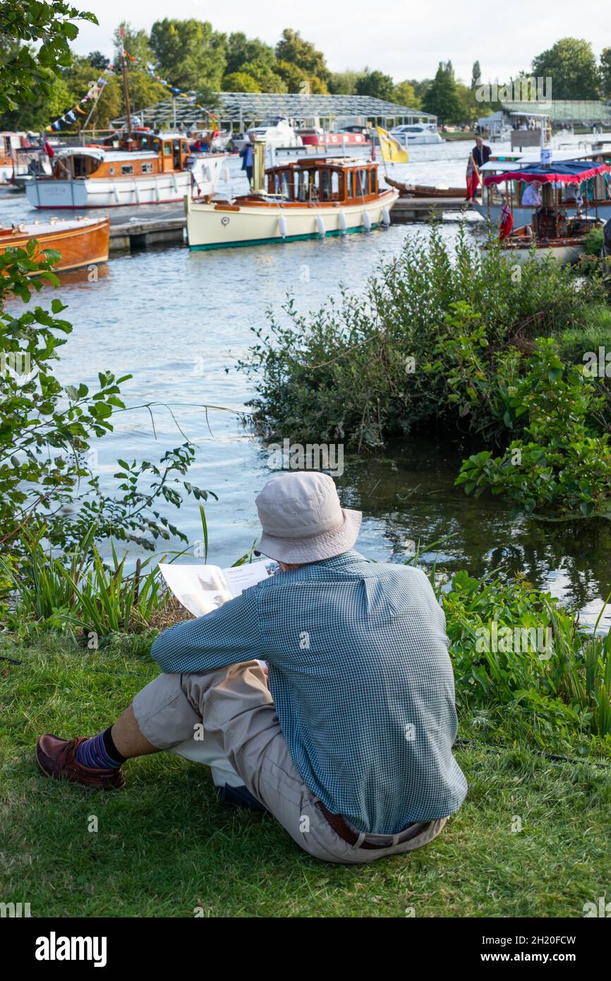 Man sitting relaxing on the Thames river bank during the Thames Traditional Boat Festival at Henley Upon Thames England Stock Photo