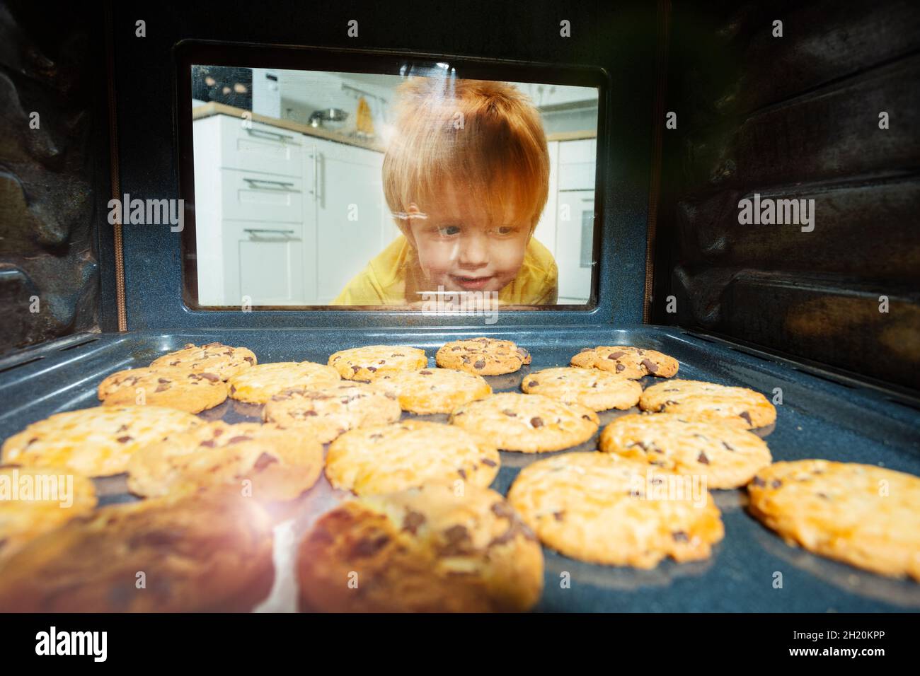 Curious boy look though oven glass at cookies Stock Photo