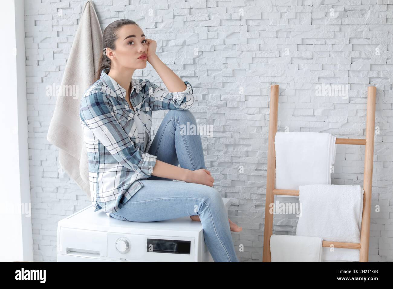 Young woman sitting on washing machine in laundry room Stock Photo Alamy