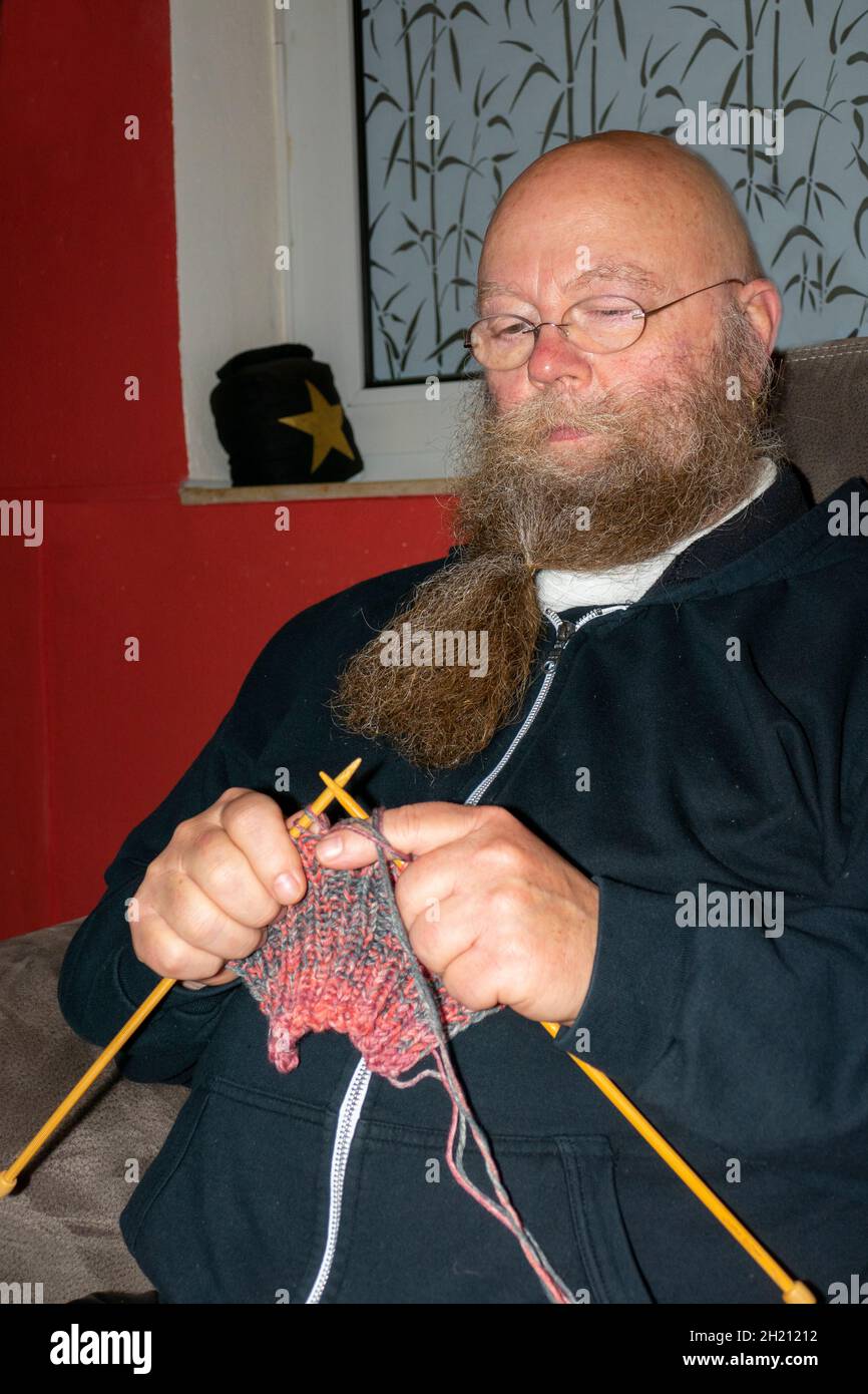 Mann mit langem Bart und Brille  strickt einen Schal Stock Photo