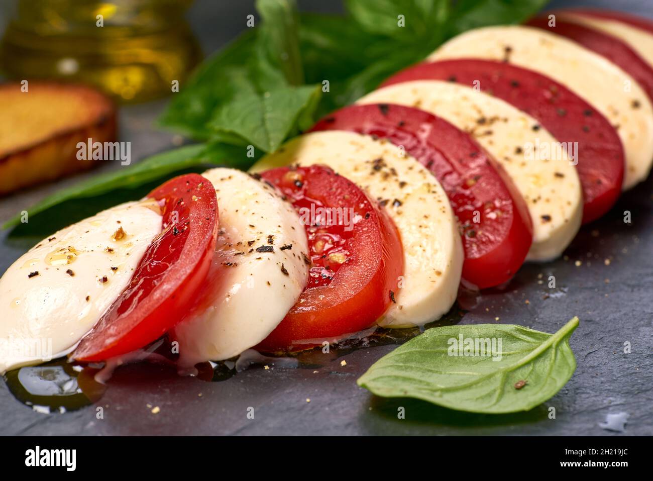 Mozzarella and tomato slices on black slate with basil and spices Stock Photo