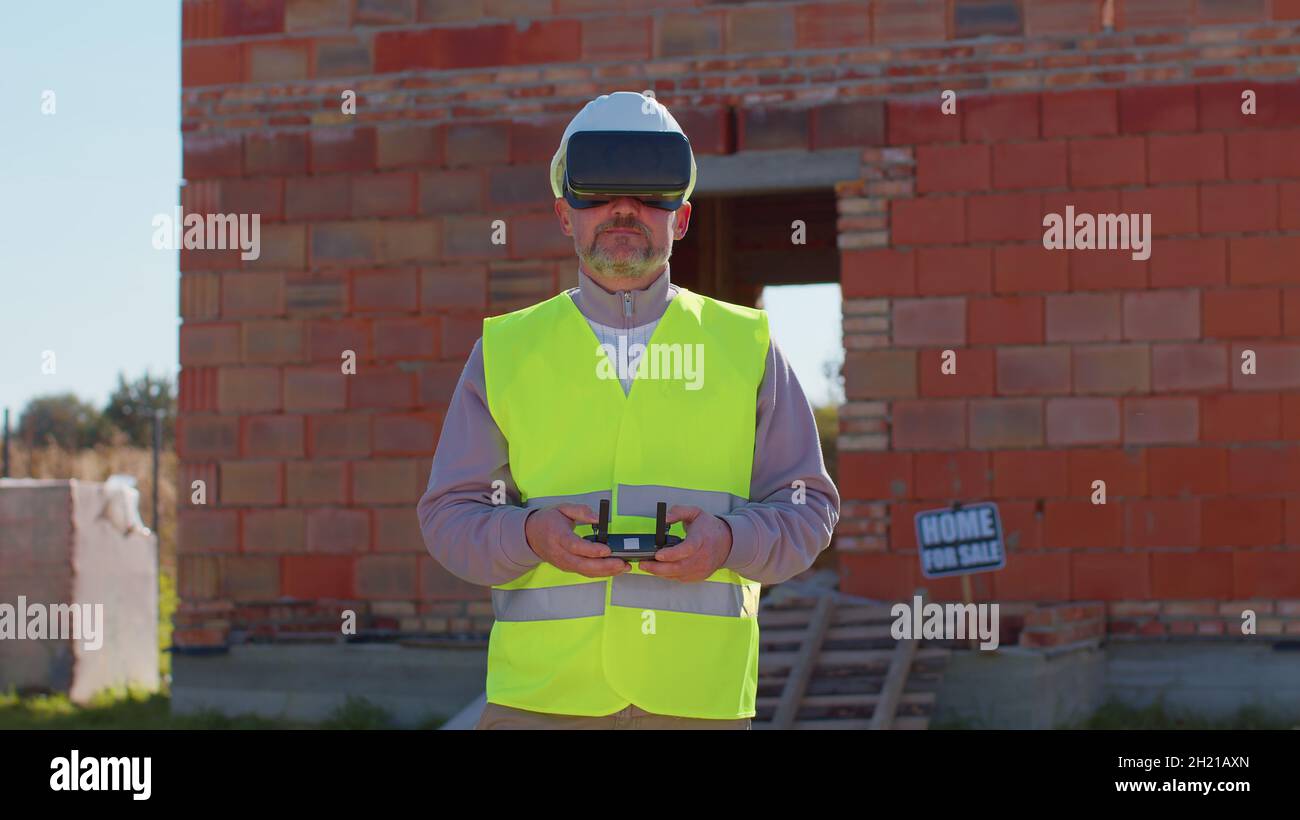 Professional builder drone operator in virtual reality helmet standing in front of construction site Stock Photo