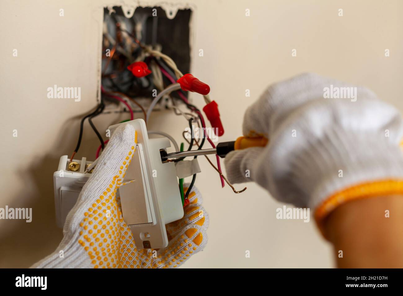 An electrician is replacing a wall switch. A DIY project concept. High voltage danger. installing wire connection using screw driver. The professional Stock Photo