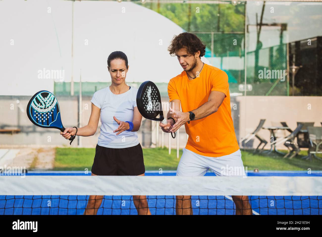Young teacher is monitoring teaching padel lesson to his student - Coach teaches girl how to play padel on the outdoor tennis court Stock Photo