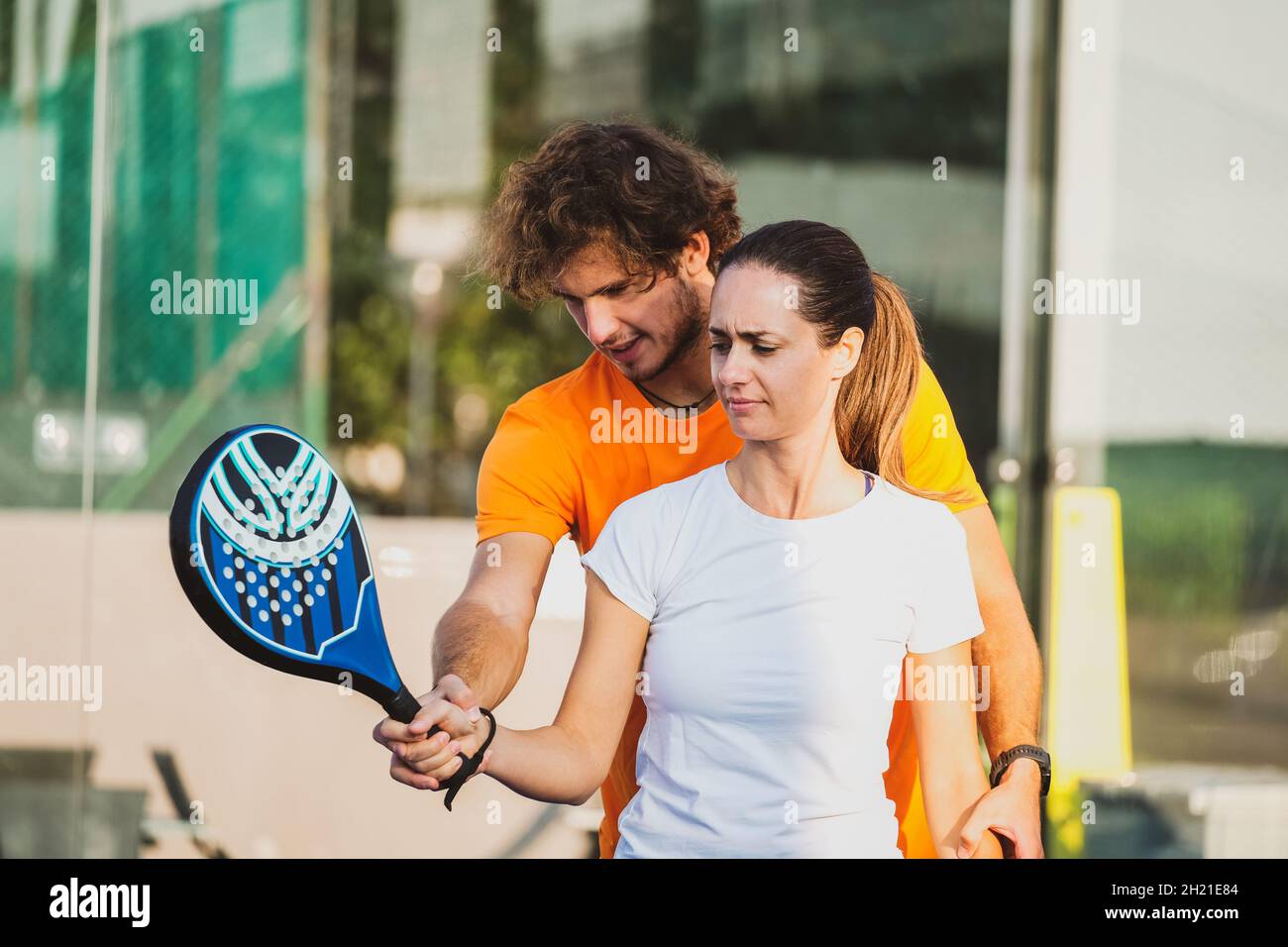 Young teacher is monitoring teaching padel lesson to his student - Coach teaches girl how to play padel on the outdoor tennis court Stock Photo