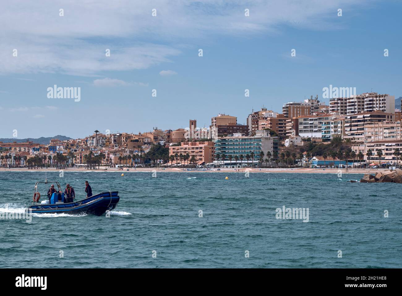 inflatable motor boat with three people entering the port of Villajoyosa with the beach and the city buildings in the background, Alicante, Spain Stock Photo